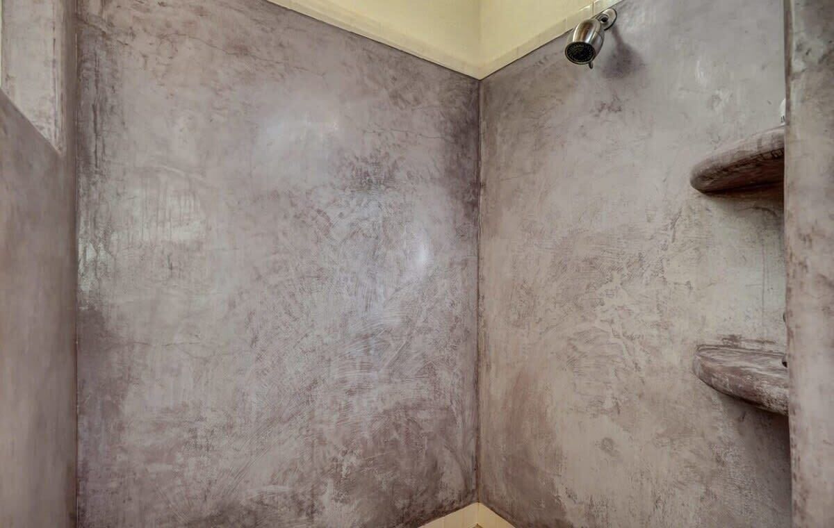 A bathroom with a textured wall, a shower area, and a wooden door.