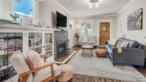 A living room with a fireplace, a sofa, a television, and a bookshelf. - 3BD Cottage Backyard near Garden of the Gods in CO (Colorado Springs)