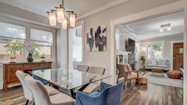 A spacious living room with a glass-top dining table surrounded by chairs, a fireplace, and a large window offering a view of the outdoors. - 3BD Cottage Backyard near Garden of the Gods in CO (Colorado Springs)