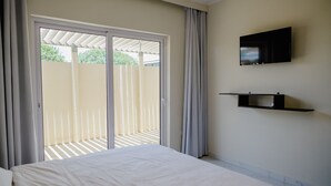 Une chambre à coucher avec un lit, un téléviseur fixé au mur et une porte-fenêtre coulissante donnant sur un balcon.
