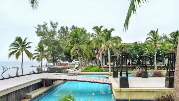 A resort pool with palm trees, a wooden deck, and a view of the sea.