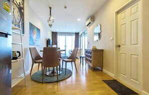 A hotel room with a dining area, a wooden cabinet, a clock, and a large window. - Luxury 2-Bedroom Condo with Ocean Views in Cha-am, Thailand (Cha-am)