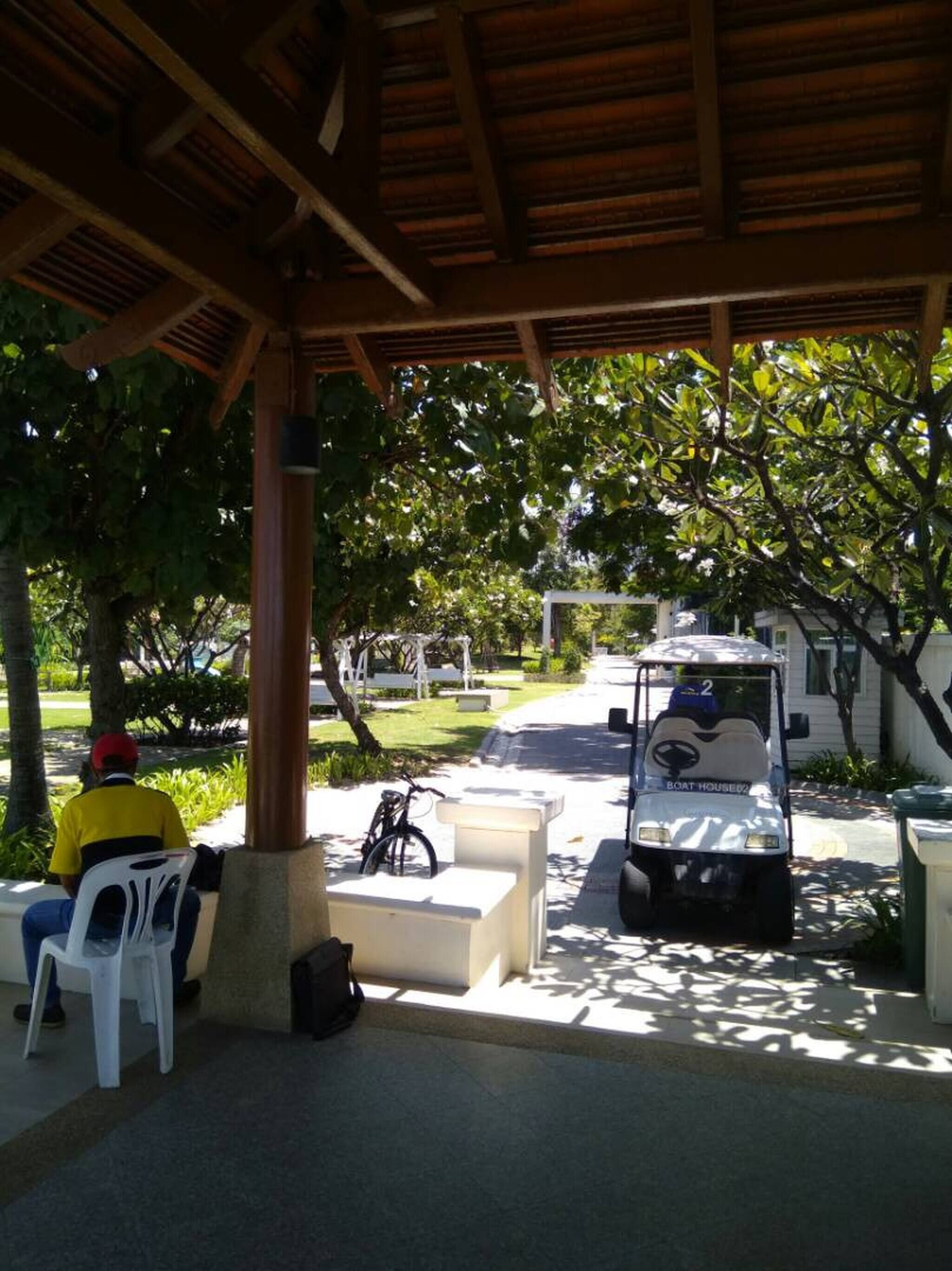 A covered outdoor seating area with a wooden roof, a bicycle, and a golf cart labeled "BOAT HOUSED".
