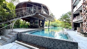 A swimming pool with a modern design, a staircase leading to a covered area, and a building with a unique architectural style. - Luxurious 4-Bedroom Apartment with Stunning Patong Bay Views (Pa Tong)
