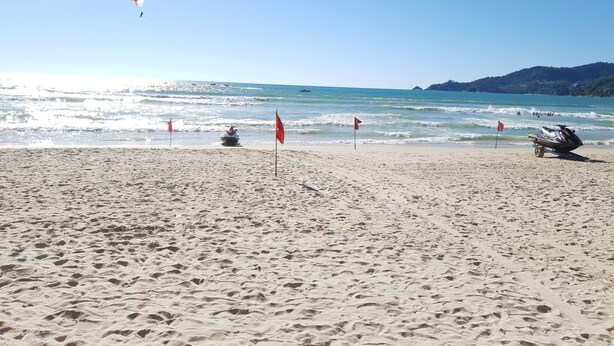 Ein Strand mit Jetski, Drachen und Flaggen im Sand.