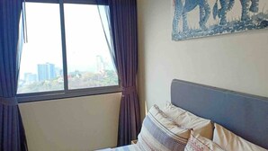 Ein Schlafzimmer mit Bett, einem Fenster mit Vorhängen und Blick auf die Stadt.