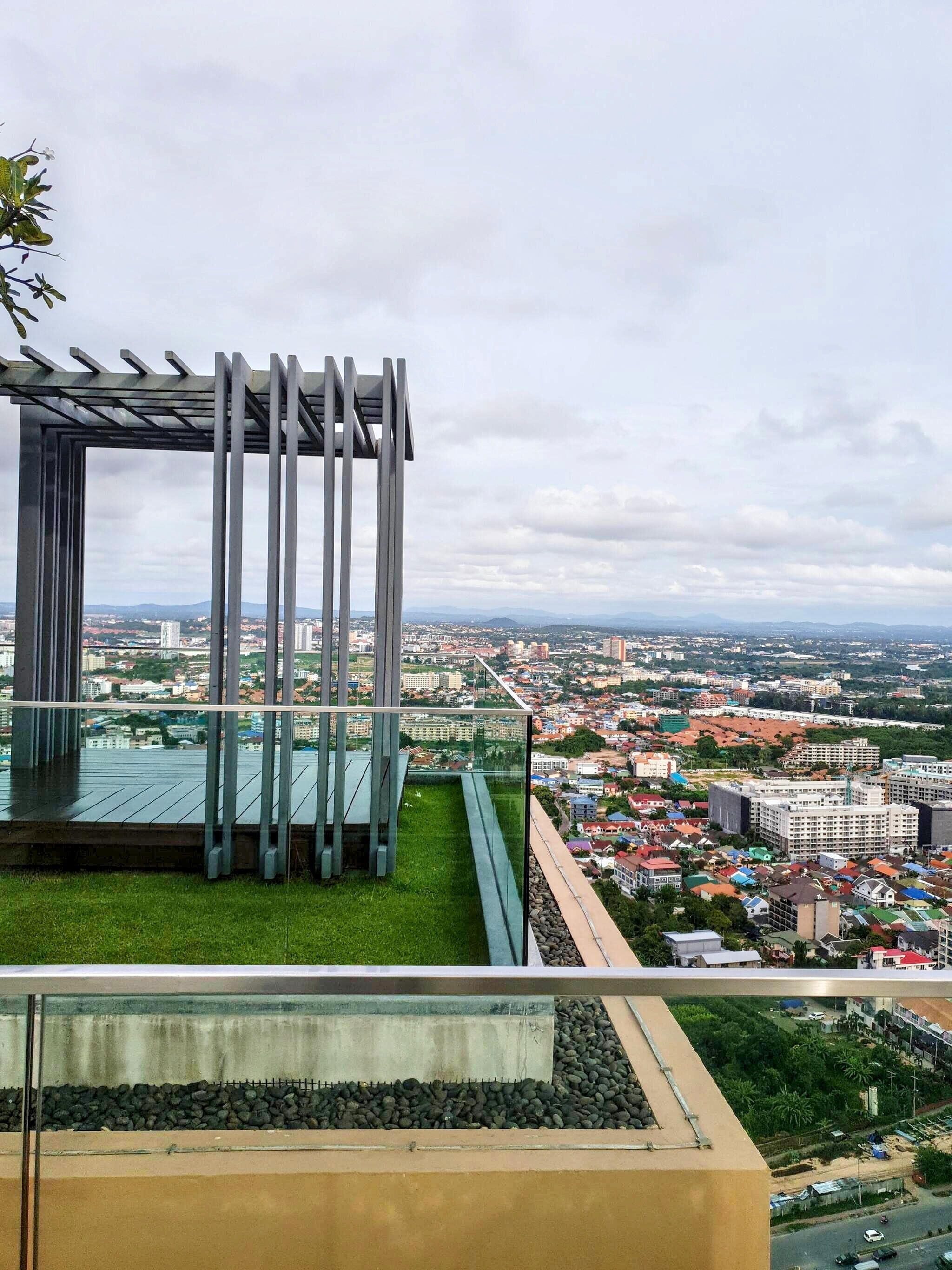 A modern building with a glass facade, a metal structure with vertical bars, and a view of a cityscape with buildings and greenery.