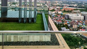 Ein modernes Gebäude mit Glasfassade, einer Metallstruktur mit vertikalen Streben und Blick auf eine Stadtlandschaft mit Gebäuden und Grünflächen.