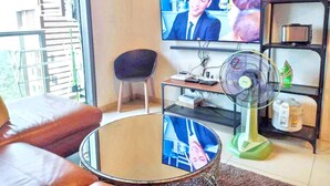 Ein Wohnzimmer mit Fernseher, Ventilator, Sessel und Sofa.