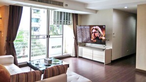 A modern living room with a large TV, a sofa, a coffee table, and a view through a large window.