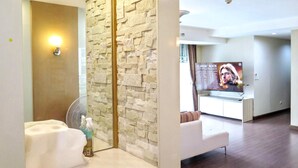 A hotel lobby with a reception desk, a wall with a stone-like texture, a fan, and a poster on the wall.