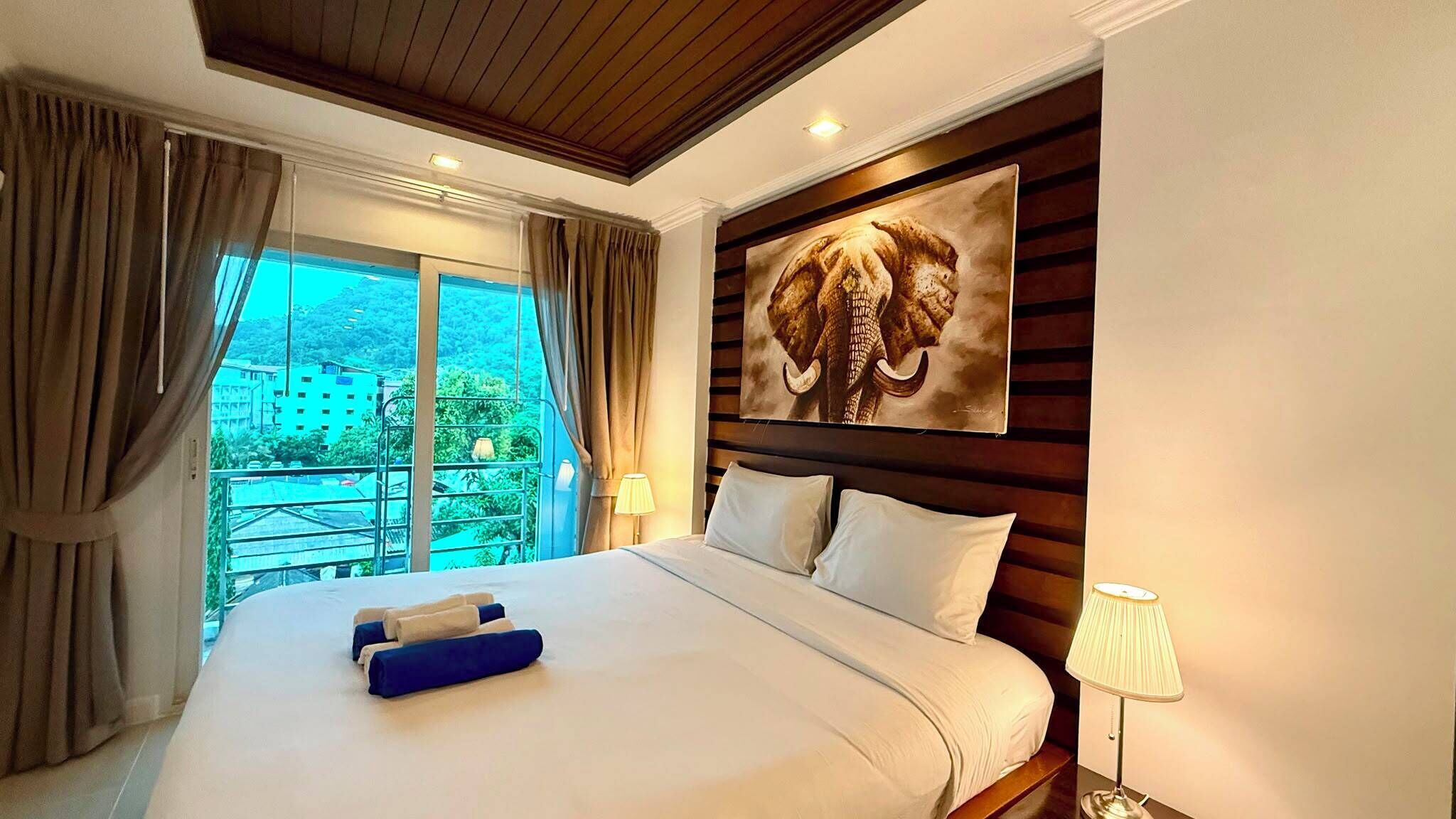 Ein Hotelzimmer mit einem großen Bett, einem Balkon mit Blick und einem Elefantenbild an der Wand.