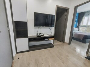 Una habitación de hotel moderna con un televisor de pantalla plana montado en la pared, un escritorio pequeño con un teléfono y una cama con cabecero oscuro.