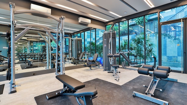 Un gimnasio moderno con diversos equipos de ejercicio, ventanas amplias y vistas a una escalera exterior.