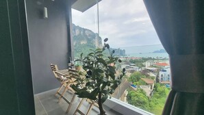 Un balcón con una mesa y sillas, una planta en maceta y vistas a la ciudad y montañas.