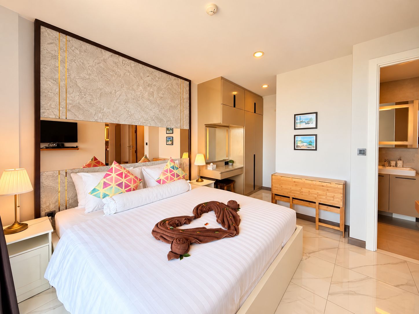 A hotel room with a large bed, a bedside table, a desk, a mirror, and a TV mounted on the wall.