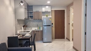 A modern kitchen with a built-in refrigerator, a dining area with a table and chairs, and a wooden door in the background. - B207 - 1 Bedroom Serviced Apartment with Pool Access at Ao Nang Beach (Tambon Ao Nang)