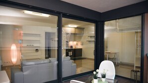A modern living area with a glass partition, a sofa, a dining table with chairs, and a small table with a potted plant. - Central Plaza Apartment 1 in Lugano (Lugano)