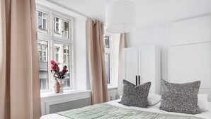 A bedroom with a bed, a window with curtains, a vase with flowers, and a white wardrobe. - City 1- Pleasant 4-Bdr Apt in Central Copenhagen (København)