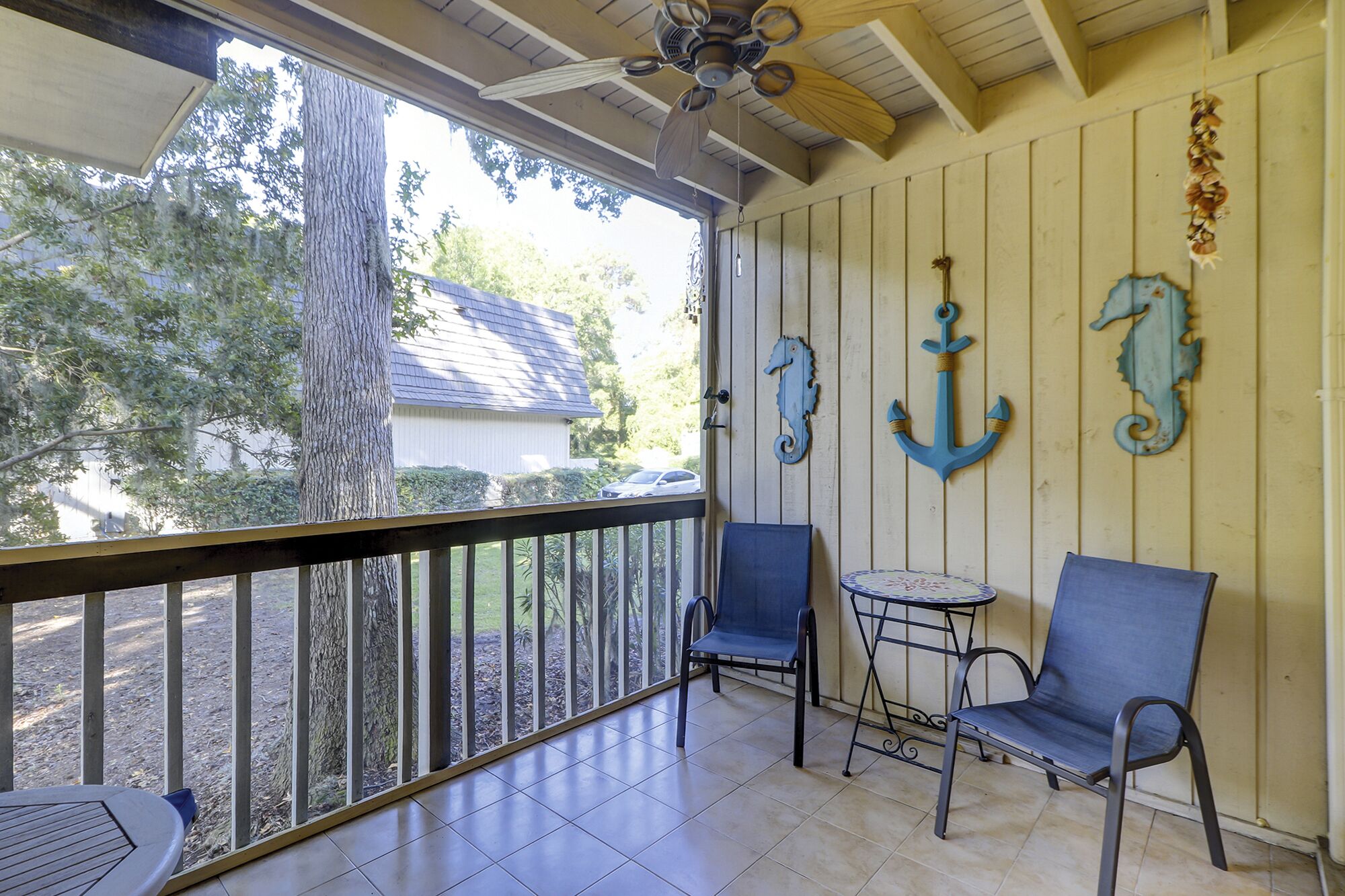 A covered porch with two chairs and a small table, wooden walls, and nautical decorations.