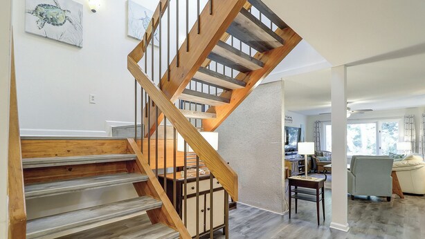 Eine Holztreppe mit Metallgeländer führt zu einem Wohnbereich mit einer Couch und einer Lampe.