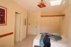 Een slaapkamer met een bed, een hanglamp, een deur en een wandplank.