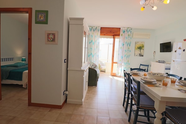 A room with a bed, a dining table with chairs, a kitchen area, and a bathroom visible through an open door.