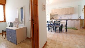 A room with a wooden wardrobe, a desk with drawers, a chair, and a dining table with chairs.