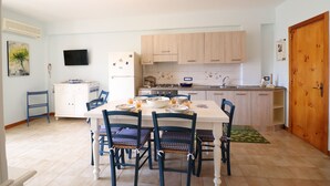 A kitchen with a dining table, chairs, cabinets, a TV, and a refrigerator.