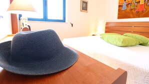 A room with a bed, a lamp, a hat, and a painting on the wall.