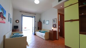 A compact living space with a sofa, a small cabinet, a television, and a door leading to an outdoor area.