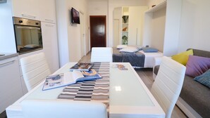 Un espacio habitable moderno y compacto con kitchenette, comedor y dormitorio.
