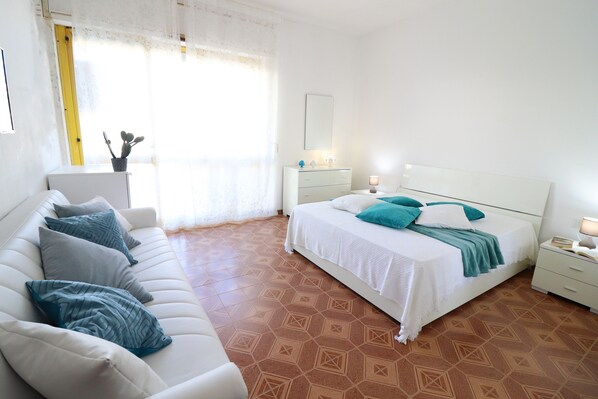 A bedroom with a bed, a sofa, a nightstand, and a window with curtains.