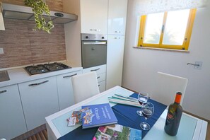 A compact kitchen with a gas stove, oven, and a window with a yellow frame. - Holiday Home 'Aurora A Otranto' with Balcony and Air Conditioning (Otranto)