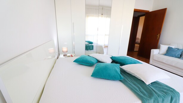 A hotel room with a bed, a white sofa, and a mirror.