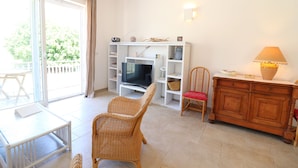 Uma sala de estar com televisão, cadeiras de vime, um armário de madeira e uma mesa.