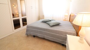 Quarto com cama, almofadas, mesa de cabeceira, abajur, guarda-roupa e espelho.