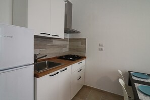 A compact kitchen with white cabinets, a stainless steel sink, a gas stove, and a built-in oven. - Casa Nausica — Elegant Apartment Facing the Aragonese Castle (Lecce)