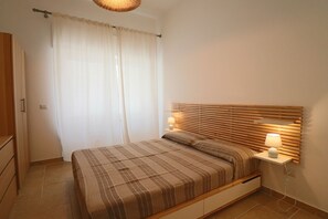 A bedroom with a bed, curtains, bedside lamps, and a wooden headboard. - Casa Nausica — Elegant Apartment Facing the Aragonese Castle (Lecce)