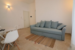 Een woonkamer met een bank, een eettafel met stoelen, een vloerkleed en een wandlamp.