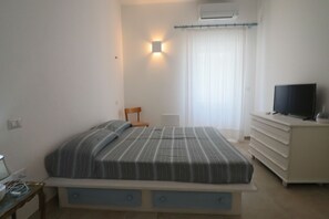 Een slaapkamer met een bed, een televisie op een dressoir en een raam met gordijnen.