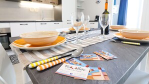 A modern kitchen with white cabinets, a microwave, and a dining table set with orange plates, glasses, and a bottle of wine. - Casa Galatea in the Center of Otranto (Otranto)