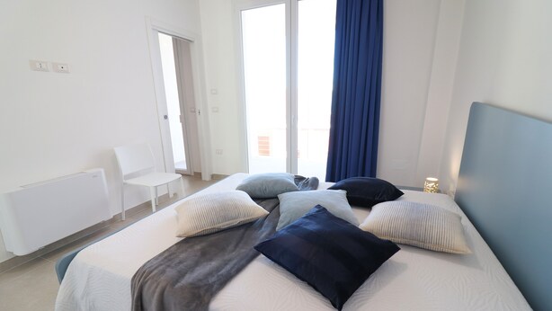 A bedroom with a bed, pillows, a chair, and a window with curtains. - Casa Galatea in the Center of Otranto (Otranto)