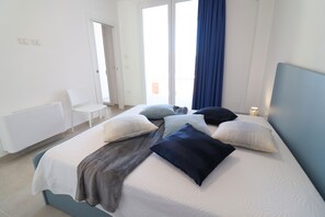 Een slaapkamer met een bed, kussens, een stoel en een raam met gordijnen.