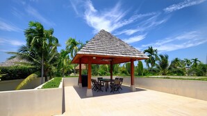 A covered outdoor seating area with a table and chairs, surrounded by palm trees and a clear sky. - Luxe 2br Pool Villa walk to Bangtao Beach (Tambon Choeng Thale)