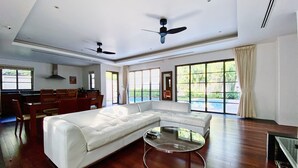 A spacious living room with a white sectional sofa, a glass coffee table, and a ceiling fan. - Luxe 2br Pool Villa walk to Bangtao Beach (Tambon Choeng Thale)