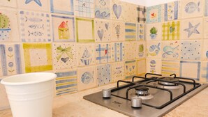 A kitchen with a gas stove and a white bucket. The wall is decorated with various colorful tiles. - Casa Sveva – Romantic studio with panoramic terrace in the heart of Otranto (Otranto)