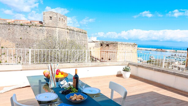 A table set for dining with a view of a historic stone wall and the sea. - Casa Sveva – Romantic studio with panoramic terrace in the heart of Otranto (Otranto)