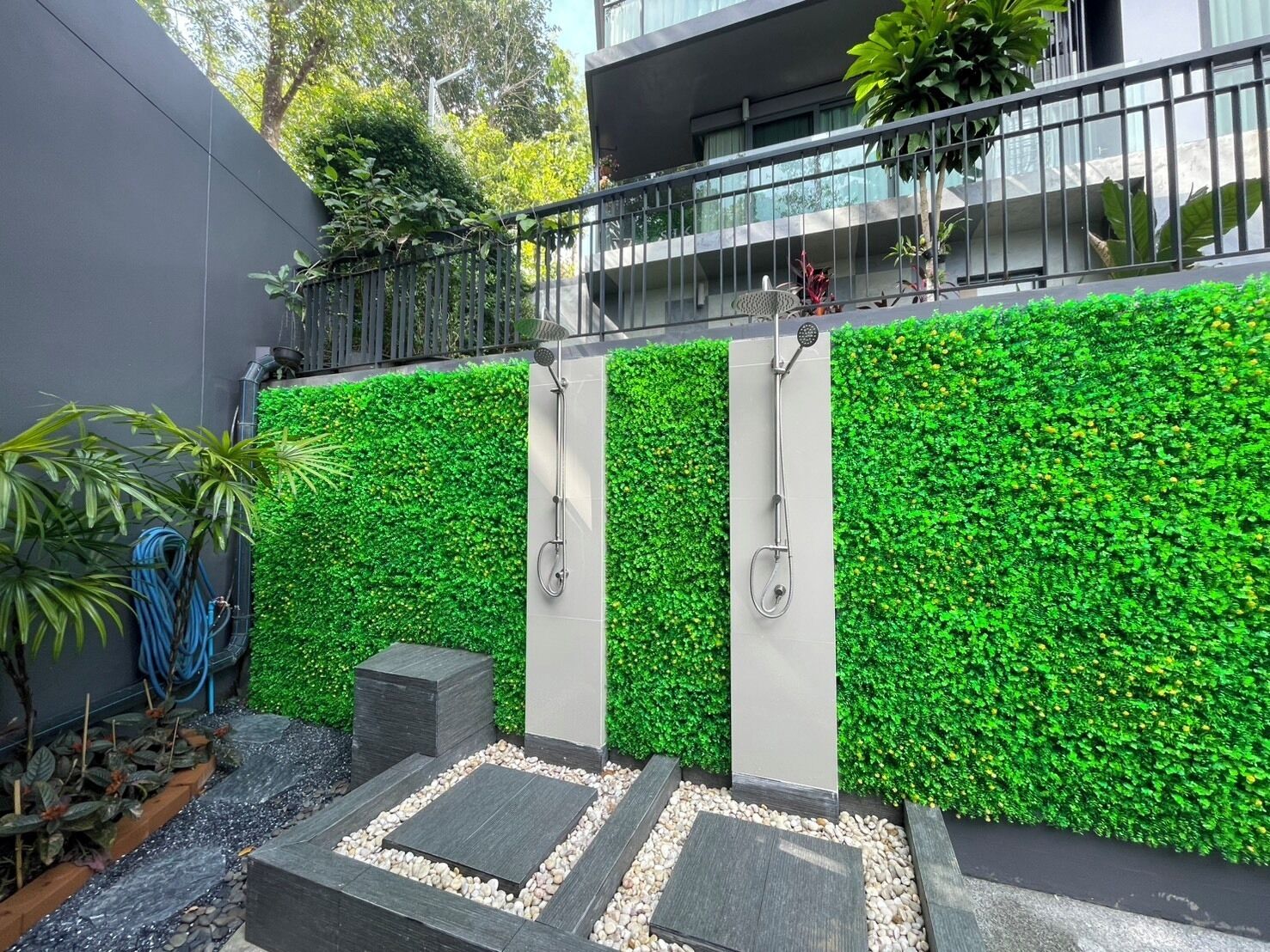 A modern outdoor shower area with a green wall, a metal railing, and a pathway with stepping stones.