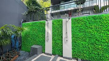 A modern outdoor shower area with a green wall, a metal railing, and a pathway with stepping stones.
